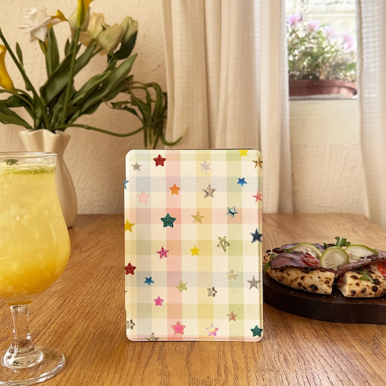 May include: A rectangular tablet case featuring a pastel-colored plaid pattern in shades of pink, yellow, blue, and green. The surface is decorated with numerous small, scattered stars in various colors, including red, blue, gold, and silver.
