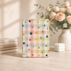 May include: A rectangular tablet case featuring a pastel-colored plaid pattern in shades of blue, pink, yellow, and green. The surface is decorated with numerous small, multi-colored star icons in various finishes, including glitter and metallic.