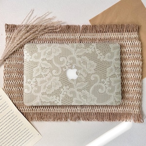 Peut inclure: Une coque rigide pour ordinateur portable ornée d'un motif floral en dentelle blanche. Le design recouvre toute la surface supérieure de l'ordinateur, mettant en valeur les détails complexes du maillage et des pétales de la dentelle.