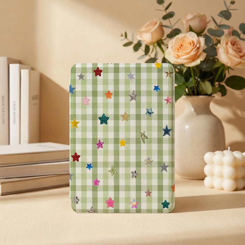 May include: A rectangular e-reader case featuring a light green and white gingham check pattern decorated with a scattered print of small, multi-colored stars in shades of red, blue, yellow, pink, and silver across the entire surface.
