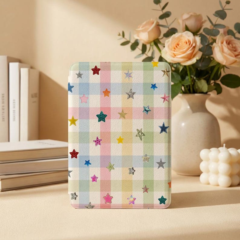 May include: A rectangular e-reader case featuring a pastel plaid pattern in shades of pink, blue, yellow, and green, decorated with scattered small stars in various colors including red, silver, gold, and blue across the entire surface.