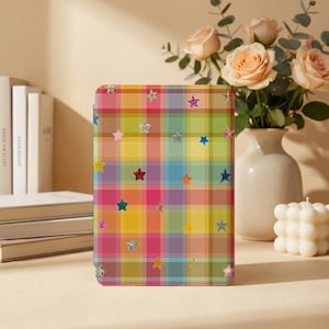 May include: A rectangular tablet case featuring a vibrant, multi-colored plaid pattern in shades of yellow, pink, blue, and green. The surface is decorated with numerous small, scattered star-shaped icons in various colors and finishes.