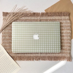 May include: A laptop with a light green and white gingham pattern. The Apple logo is visible on the laptop. The laptop is on a woven brown placemat with a fringed edge. Dried wheat stalks are on the left.