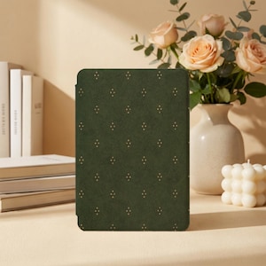 May include: A dark green e-reader cover featuring a repeating pattern of small gold-colored dots arranged in diamond shapes. The cover has a textured, matte finish and is rectangular in shape with rounded corners, providing a protective exterior.