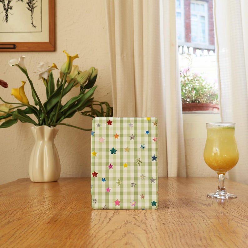 May include: A rectangular e-reader case featuring a light green and white gingham check pattern decorated with small, scattered, multi-colored star icons in shades of red, blue, yellow, pink, and silver across the front surface.