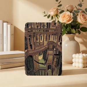May include: A rectangular e-reader cover featuring a detailed illustration of a multi-level library with ornate wooden railings, tall bookshelves, and a large black bird flying through the center of the architectural space in shades of brown and gold.