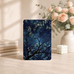 Puede incluir: Una funda rectangular para tableta con un fondo azul marino oscuro y una ilustración detallada de ramas de árbol cubiertas de pequeñas flores de color azul claro y blanco. El diseño cubre toda la superficie frontal de la funda protectora.
