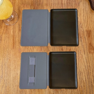May include: Two open gray e-reader cases are displayed. Each case features a smooth gray exterior cover and a black interior frame with a textured, dotted pattern. The bottom case includes a vertical gray elastic strap attached to the inner cover.