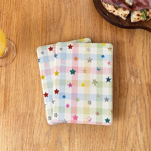 May include: Two rectangular coasters featuring a pastel-colored gingham check pattern in shades of light blue, pink, yellow, and green. The surface is decorated with numerous small, multi-colored star shapes scattered across the grid design.