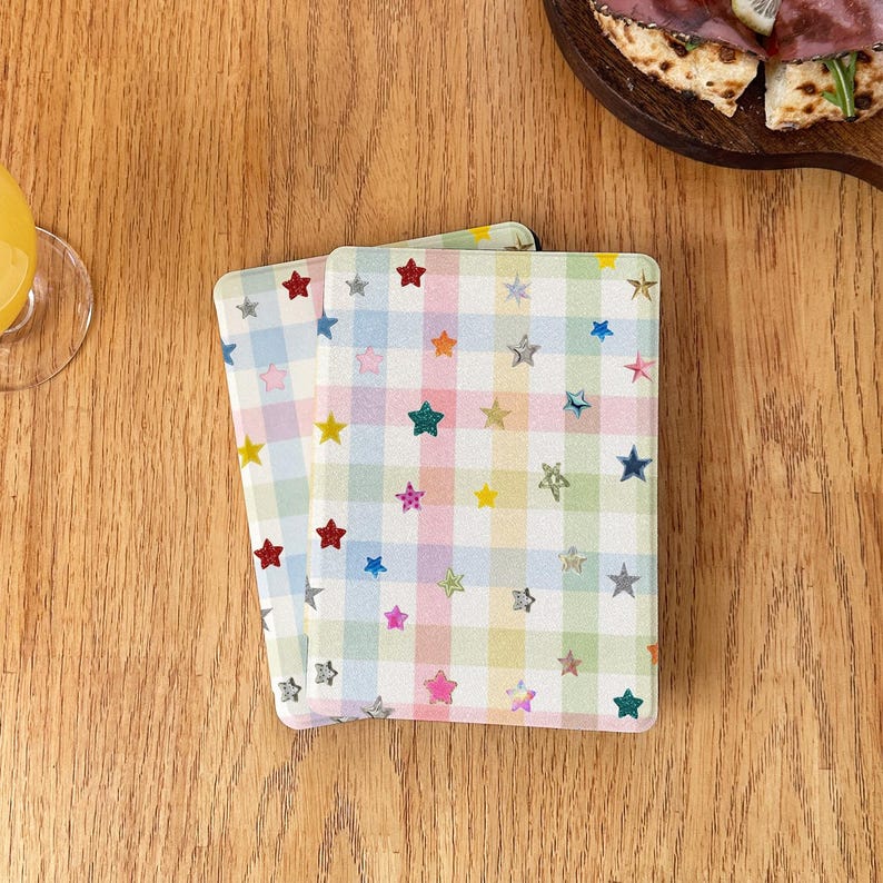 May include: Two rectangular coasters featuring a pastel-colored gingham check pattern in shades of light blue, pink, yellow, and green. The surface is decorated with numerous small, multi-colored star shapes scattered across the grid design.