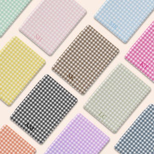 May include: A collection of personalized notebooks with a gingham pattern in various colors, including pink, blue, yellow, and brown. Each notebook features initials in the corner. The notebooks are arranged in a diagonal pattern.