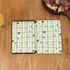 May include: A rectangular e-reader case featuring a light green and white gingham check pattern decorated with scattered, multi-colored glittery stars in shades of red, blue, yellow, pink, and silver across the entire surface.