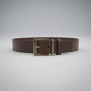 May include: A brown leather belt with a rectangular, antique brass buckle. The belt is a medium brown color and appears to be made of textured leather. The buckle is a square shape with a single prong.