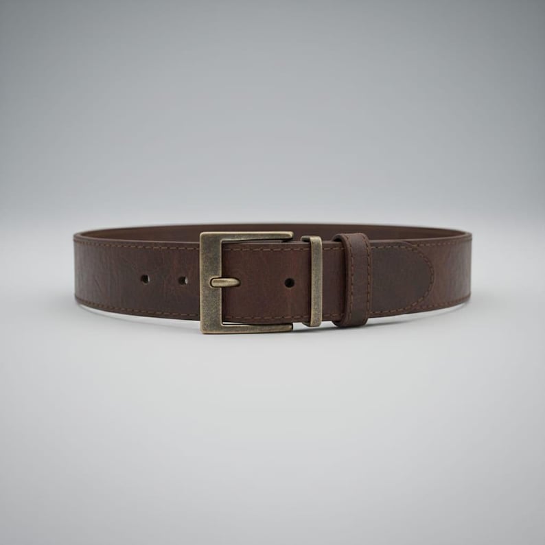 May include: A brown leather belt with a rectangular, antique brass buckle. The belt is a medium brown color and appears to be made of textured leather. The buckle is a square shape with a single prong.