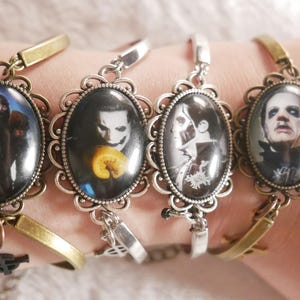 May include: Four silver charm bracelets with round glass cabochons featuring black and white images of men's faces. The bracelets are on a person's wrist.
