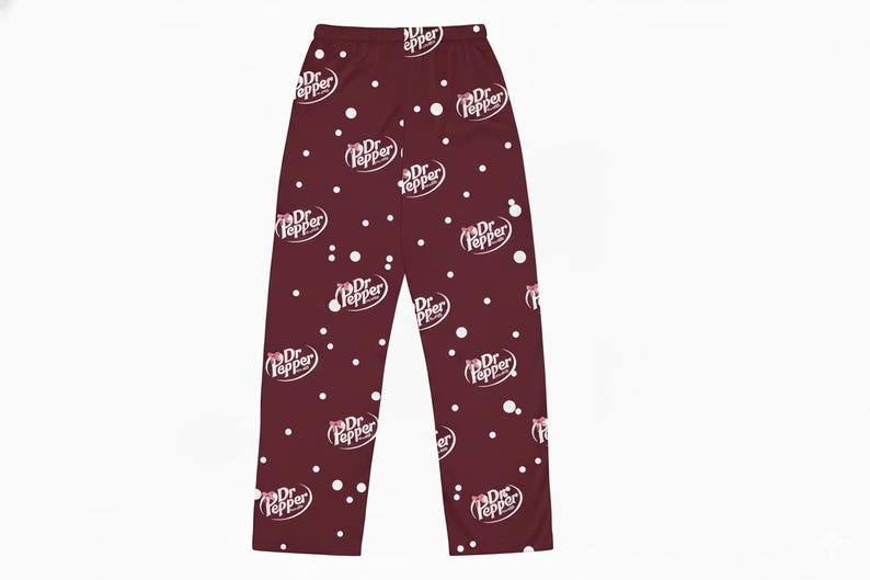 May include: Burgundy pajama pants with a repeating pattern of the Dr Pepper logo and white polka dots. The Dr Pepper logo is in white with a red bow. The pants are made of a soft material.