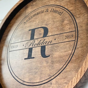 Puede incluir: Una bandeja redonda de madera con asas de metal dorado. La bandeja tiene un c&iacute;rculo negro en el centro con el texto "Annamarie & Daniel" y "ESTD. Roldan. 2019" en una fuente cursiva.