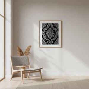 May include: A framed artwork featuring a black and silver damask pattern. The ornate design is set against a dark background, creating a striking contrast. The artwork is displayed in a light-colored wooden frame, adding a touch of elegance to the room's decor.