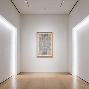 Op de afbeelding: Een ingelijst textielkunstwerk met een geometrisch blauw-wit ontwerp hangt aan een witte muur in een galerie. Het rechthoekige kunstwerk heeft een houten frame en franjes aan de onderkant. De kamer heeft een houten vloer en inbouwverlichting.