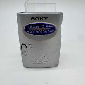 以下が含まれることがあります： シルバーカラーのソニー製FM/AMラジオ、ウォークマンSRF-59。青いチューニングディスプレイに周波数が表示され、電源のオン・オフスイッチとウォークマンのロゴが、コンパクトな長方形のプラスチック製本体の前面にプリントされています。