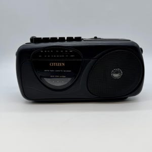 May include: A black Citizen AM/FM radio cassette recorder. The radio features a speaker on the right and a dial with radio frequency numbers. The text "CITIZEN" and "AM/FM RADIO CASSETTE RECORDER" are visible on the front.