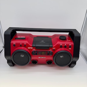 May include: A red Sony portable CD player and radio boombox with a black handle and speaker grilles. The device features a top-loading CD compartment, a central digital display, volume control, and various playback buttons labelled MP3 and Sony.