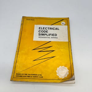 Peut inclure: Un livre jaune intitulé "ELECTRICAL CODE SIMPLIFIED RESIDENTIAL WIRING". Le livre est basé sur la 21e édition du Code de sécurité électrique de l'Ontario. La couverture comporte une étiquette blanche avec du texte noir et un éclair.