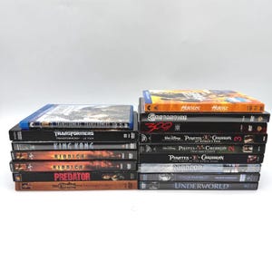 Op de afbeelding: Een stapel dvd's en Blu-ray discs met filmtitels als "Transformers", "King Kong", "Riddick", "Predator", "Hercules" en "Pirates of the Caribbean". De hoezen tonen kleurrijke illustraties.