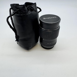 Puede incluir: Un objetivo de cámara Bushnell negro con una bolsa con cordón negra a juego. El objetivo tiene un agarre acanalado y el nombre de la marca está impreso en la parte superior. La bolsa está hecha de un material suave similar al cuero.