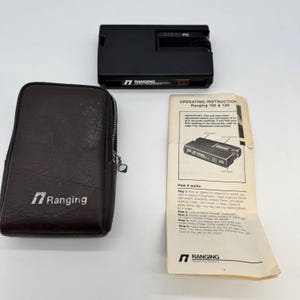 Peut inclure: Un télémètre noir Ranging 100 avec un étui en cuir marron et un manuel d'instructions. Le télémètre porte l'inscription "Ranging 100". Le manuel porte l'inscription "Operating Instructions Ranging 100 & 120".