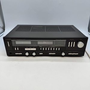 May include: A black Technics SA-222 stereo receiver featuring a digital display showing 96.30, multiple silver control knobs, push buttons, and a ventilation grille on the top panel. The front panel includes various input and tuning controls.