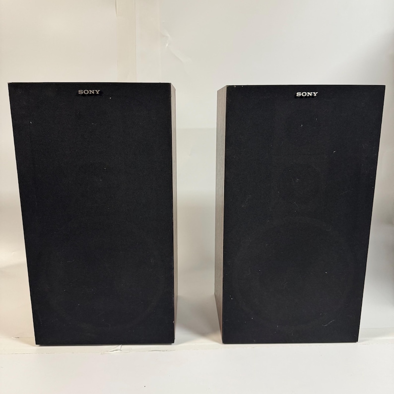 May include: Two black Sony speakers. Each speaker is a rectangular box with a circular speaker visible on the front. The word "SONY" is printed in white on the top of each speaker.