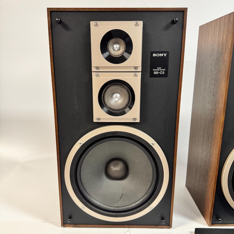 May include: Vintage Sony SS-C3 speaker system. The speaker has a black front with a large circular speaker and two smaller square speakers. The speaker is framed in dark wood. The Sony logo and model number are visible.
