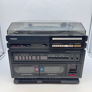 May include: A black Toshiba stereo system, including a turntable, digital tuner, and cassette player. The unit has a clear plastic cover over the turntable. It features buttons and dials. The model number SL-3147 is visible. The system is a vintage audio device.