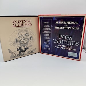 May include: Two square vinyl record box sets. The left box is cream-coloured with a black line drawing of Arthur Fiedler and the text An Evening at the Pops. The right box is dark blue with white text reading Arthur Fiedler and the Boston Pops.
