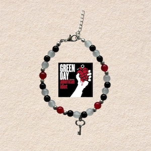Può includere: Un braccialetto di perline nere, rosse e bianche. Il braccialetto include un ciondolo con la scritta "GREEN DAY american idiot" e un ciondolo a forma di chiave. Il braccialetto è in metallo color argento.