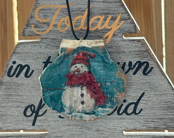 Simpático muñeco de nieve sobre fondo azul con una bufanda de cristal rojo, adorno navideño decoupage.