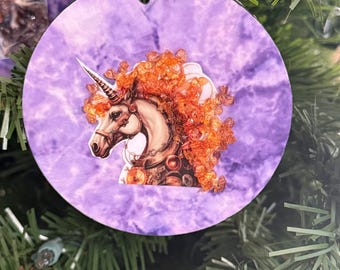 Adorno navideño de unicornio. Melena de cristal naranja sobre fondo morado.