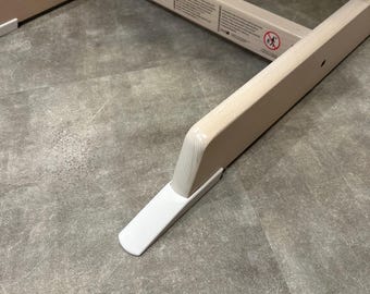 May include: A light-colored wooden frame structure featuring two parallel base rails with white plastic extensions at the ends. A horizontal crossbar connects the rails, displaying printed safety warning text and a circular no-climbing icon.