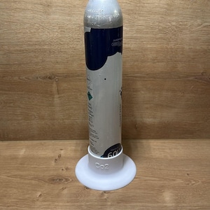 Könnte beinhalten: Ein silberner und blauer CO2-Zylinder, der aufrecht in einem weißen, runden Kunststoffsockel steht. Der Zylinder hat eine gelbe Kappe an der Oberseite, eine blaue Umhüllung im oberen Bereich und aufgedruckten Text, einschließlich der Aufschrift 60L auf dem Sockel.