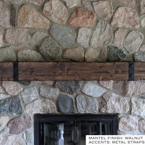 May include: A rectangular wooden mantel with a walnut finish, featuring two black metal straps on the left and right sides, each secured with two circular black buttons. The text on the image reads: MANTEL FINISH: WALNUT ACCENTS: METAL STRAPS/BUTTONS.