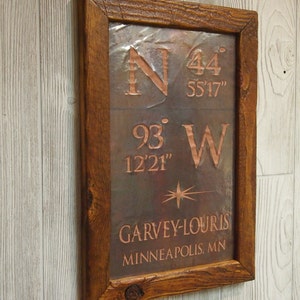 May include: A wooden framed sign with a copper plate featuring the coordinates 44° 55'17" N 93° 12'21" W and the text "GARVEY-LOURIS MINNEAPOLIS, MN".