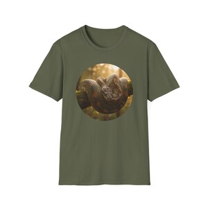 Peut inclure: T-shirt vert olive avec un motif circulaire d'un serpent enroulé. Le serpent est brun et beige, avec des motifs détaillés. L'arrière-plan est flou avec la lumière du soleil, créant une scène naturelle.