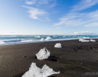 Könnte beinhalten: Eine Küstenlandschaft mit schwarzem Sandstrand und Eisformationen. Das Meer trifft auf den Strand unter blauem Himmel mit Wolken. Das Bild ist ein Kunstdruck, der eine natürliche Szene einfängt.
