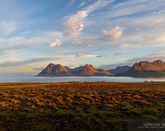 Könnte beinhalten: Landschaftsfotografie mit einer Bergkette unter einem teilweise bewölkten Himmel. Die Berge werden von der Sonne beleuchtet, mit einem Gewässer und einem Feld im Vordergrund. Das Bild hat einen warmen, goldenen Farbton.