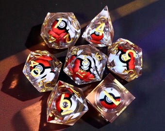 May include: Set of seven polyhedral dice with a clear, faceted design. Each die features a red and white design with gold numbering. The dice are arranged on a dark surface, showcasing their unique design.