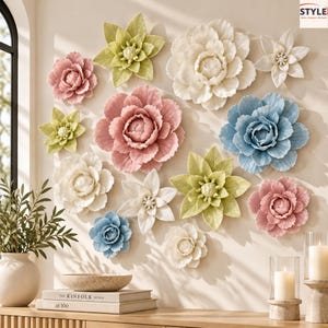 May include: A collection of thirteen ceramic flower wall decorations in various sizes and colours, including shades of pink, white, blue, and light green. The flowers feature layered petals and are arranged on a wall. A logo reads STYLE.