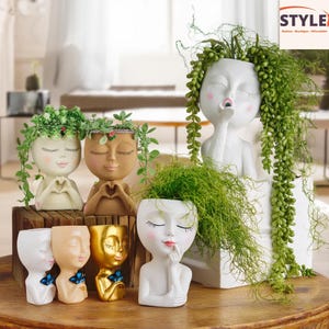 以下が含まれることがあります： 白、ベージュ、金など、さまざまな色の顔型プランターのコレクション。 プランターは目を閉じ、頬を赤らめ、緑で満たされています。 一部のプランターには蝶のデザインがあります。