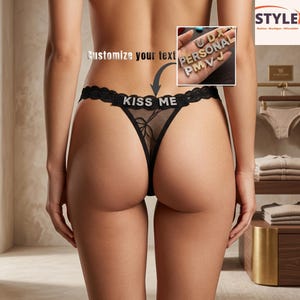 May include: Black thong underwear with a delicate lace design and the text "KISS ME" in silver lettering. The underwear features a bow detail and a sheer mesh panel. The image also shows customizable letter charms.