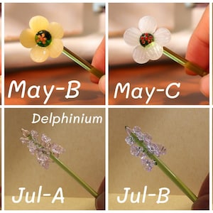 May include: A collection of handcrafted glass flower stems, each featuring a different flower design. The flowers include a yellow Hawthorn, a white flower, a red Rose, and Delphinium. Each stem is held by a hand, with text labels.